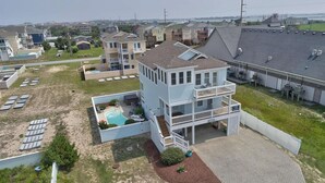 A multi-story building with a pool, surrounded by other residential structures. - 🏖️1 min to beach access!🏊‍♂️Heated pool, hot tub, pets, ocean views, arcade! (Nags Head)