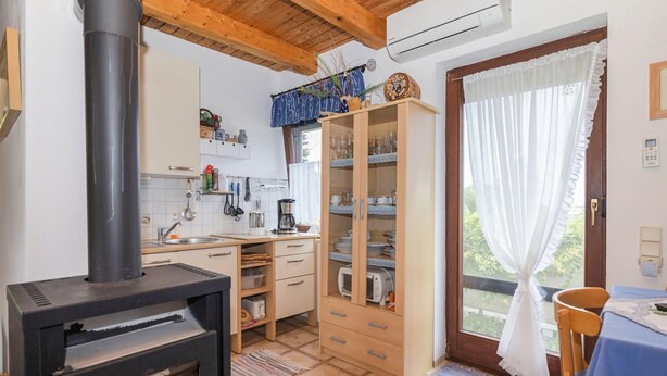 Una cocina con estufa de leña, armarios y una ventana con cortinas.