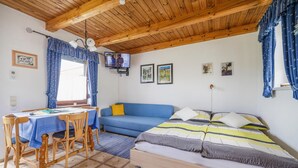 Una habitación acogedora con techo de madera, un sofá azul, una cama con ropa de cama a rayas, una mesa de comedor con sillas y un televisor en la pared.