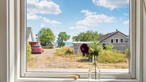Uitzicht vanuit een raam op een landelijk gebied met een onverharde weg, een rode auto en een houten huis.