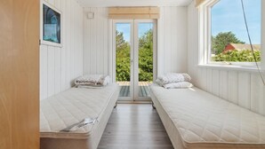 Een kleine, gezellige kamer met twee enkele bedden, een raam met uitzicht op groen en een deur naar buiten.
