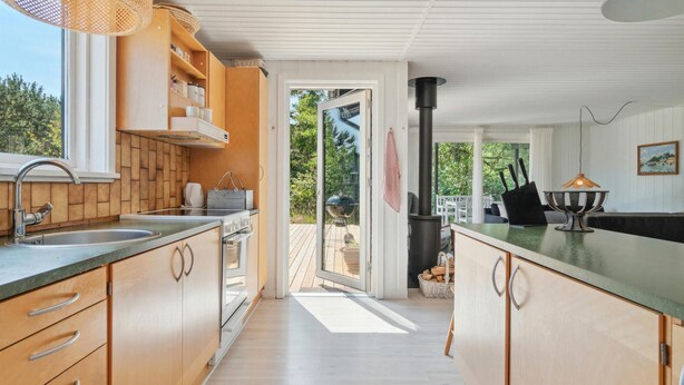 Een moderne keuken met houten kasten, een roestvrijstalen spoelbak en een groot schiereiland. Buiten de deur is er een grill en een eethoek met een tafel en stoelen.