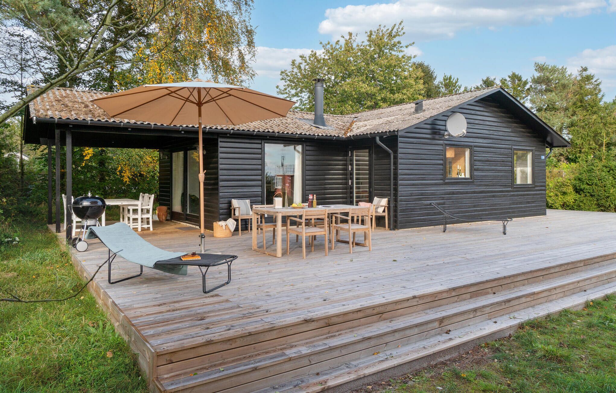Una cabaña con terraza, mobiliario exterior y una parrilla.