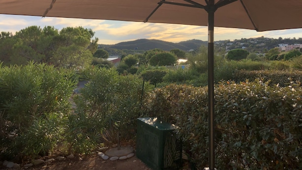 A patio area with a large umbrella, surrounded by various plants and a view of distant hills. - Nouvel Grand Studio Agay vue mar Avec Jardin (Saint-Raphaël)