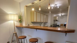 A kitchen with a wooden countertop, three stools, a hanging light fixture, and a large mirror above the counter. - Beautiful 1-bed Apartment in Manchester (Manchester)