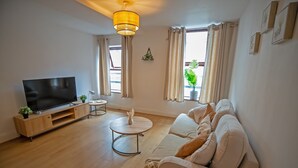 A modern living room with a flat-screen TV, a sofa, a coffee table, and a pendant light. - Beautiful 1-bed Apartment in Manchester (Manchester)