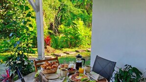 Ein Essbereich im Freien mit einem für das Frühstück gedeckten Tisch, umgeben von Stühlen und Blick auf einen üppigen Garten.