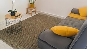Ein Wohnzimmer mit einer Couch, einem kleinen Tisch mit einer Vase, einer Topfpflanze, einer Wanduhr und einem gerahmten Bild.