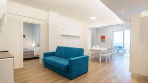 A modern hotel room with a blue sofa, a dining area with white chairs, and a balcony with a view. - Nice apartment in Pineto with swimming pool (Pineto)