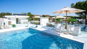 A swimming pool with clear blue water, surrounded by white lounge chairs and umbrellas, and a modern building in the background. - Nice apartment in Pineto with swimming pool (Pineto)