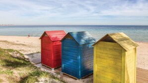 Drie strandhutten in rood, blauw en geel, gelegen op een zandstrand met de zee op de achtergrond.