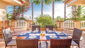 Een zonnig terras met een tafel voor vier personen, omringd door rieten stoelen en een witte balustrade.
