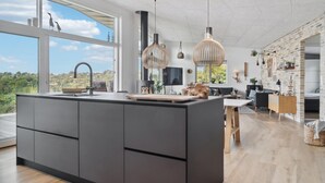Moderni keittiö, jossa on suuri keittiösaareke, suuret ikkunat ja näkymä maaseudulle.