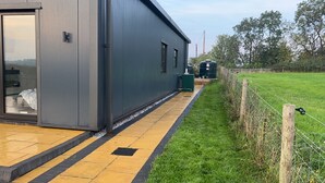 A modern building with a large glass door, a paved walkway, and a grassy area with a fence. - Beautiful 3-bed Barn in Uttoxeter (Uttoxeter)