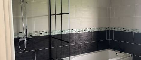 Une salle de bain moderne avec une baignoire, un espace douche et des murs carrelés.