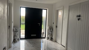 A hallway with a black door, white walls, and marble flooring. There are two vases with white flowers on either side of the door. - Beautiful 3-bed Barn in Uttoxeter (Uttoxeter)