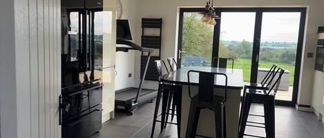 A modern kitchen with a dining area, large windows, and a view of the outdoors.