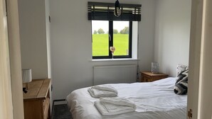 A bedroom with a bed, a window with a view of a green field, a bedside table with a lamp, and a radiator. - Beautiful 3-bed Barn in Uttoxeter (Uttoxeter)