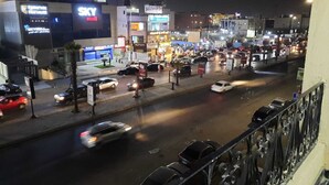 Una animada calle urbana de noche con varios edificios comerciales, incluyendo un centro comercial SKY y un banco.