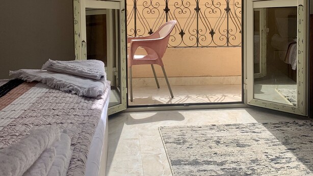 Un dormitorio con cama, una silla y puerta abierta al balcón.