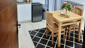 Cocina compacta con refrigerador, un lavamanos y un pequeño cubo de basura. Hay una mesa de comedor con cuatro sillas y un florero con flores.
