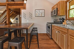 Una cocina con armarios de madera, estufa de acero inoxidable, microondas y un fregadero. Hay taburetes y una mesa de madera.