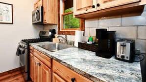 Una cocina con armarios de madera, un lavamanos de acero inoxidable, una estufa, un microondas, una cafetera y un tostador.