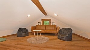 Una habitación acogedora en el ático con un sofá de cuero marrón, dos sillones de felpa y una pequeña mesa redonda.