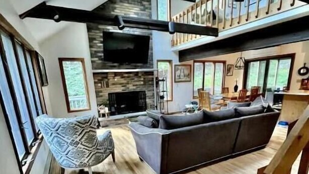 A spacious living area with a large dark-colored sofa, a patterned chair, and a hammock. A fireplace is visible in the background, and the room has a high ceiling with exposed beams. - Retreat to Jackson's Ridge and enjoy the Poconos! (East Stroudsburg)