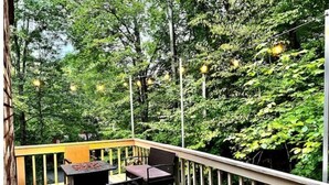 A deck with a fire pit, two chairs, and a table, surrounded by lush greenery and string lights. - Retreat to Jackson's Ridge and enjoy the Poconos! (East Stroudsburg)