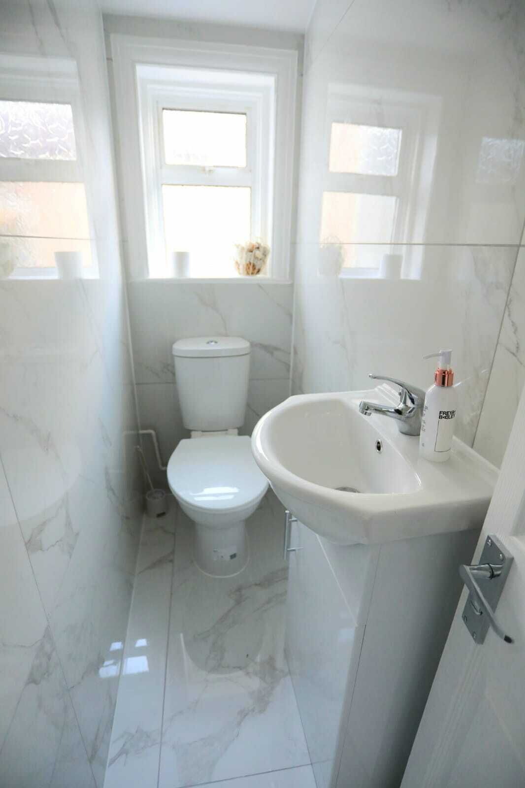 Een kleine, moderne badkamer met toilet, wastafel en raam.