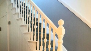 Una escalera con balaustres blancos y un rellano cubierto de alfombra oscura.