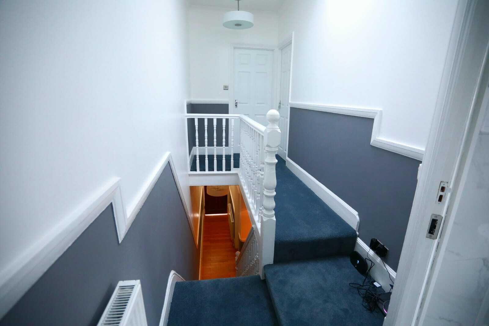 A narrow stairway with a wooden handrail and a white door at the top.