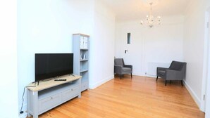 Una sala de estar moderna con un televisor de pantalla plana sobre un mueble de madera, sillones grises y una araña.