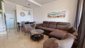 A living room with a sectional sofa, a glass coffee table, and a dining area with chairs and a table.