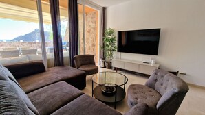 A modern living room with a sofa, armchairs, a glass coffee table, and a flat-screen TV. - Cozy apartment with Jacuzzi/ fast WIFI/PS5/huge pool and kids pool. Family place (CN)