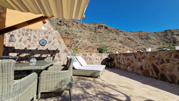 An outdoor patio with wicker furniture, a dartboard, and a stone wall.