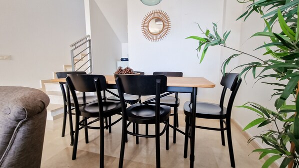 A dining area with a wooden table and four black chairs, a decorative mirror on the wall, and a staircase in the background.