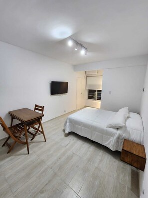 Un dormitorio con cama, televisión, mesa y sillas, y aire acondicionado.