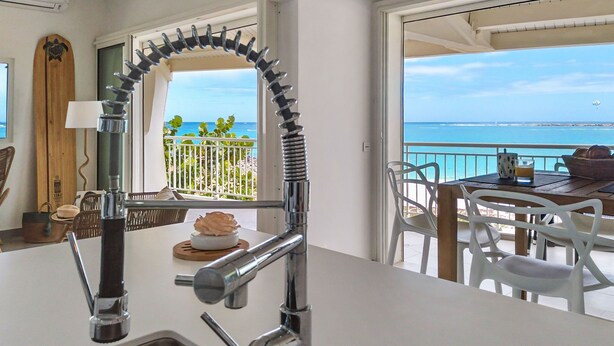 Une cuisine dotée d’un robinet moderne, un coin repas avec une table et des chaises, et une vue sur l’océan depuis un balcon.