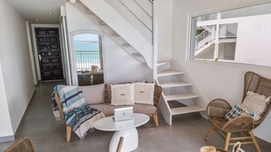 Un salon moderne avec un canapé, deux fauteuils en osier, une table basse et un escalier.