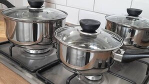 Uma cozinha com panelas de aço inoxidável em um fogão, uma tábua de corte de madeira e um conjunto de facas sobre o balcão.