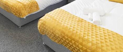 Two twin beds with matching yellow and white bedding, grey headboards, and a grey carpet.