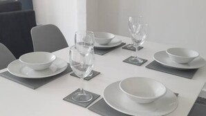 Mesa de jantar moderna com pratos, tigelas e copos de vinho brancos, rodeada por cadeiras cinzentas.