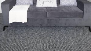 Um sofá cinzento com almofadas estampadas e um cobertor branco.