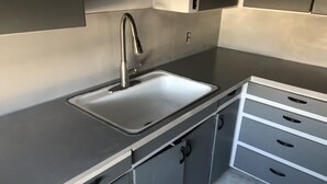 A kitchen with a stainless steel sink, a faucet, and a countertop. There are three drawers and a cabinet below the countertop.