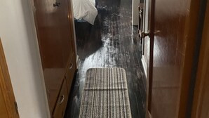 A narrow hallway leading to a bedroom with a bed, a door, and a mat on the floor.