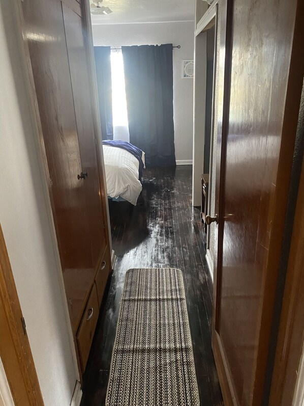 Un pasillo estrecho que conduce a un dormitorio con cama, una puerta y un felpudo en el suelo.