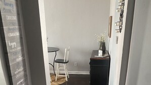 A hallway with a dark wooden floor, a rug, a dining table with chairs, and a small side table with a vase.