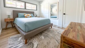 Ein Schlafzimmer mit Bett, Nachttischen, Deckenventilator, großem Spiegel und einem Holztisch.